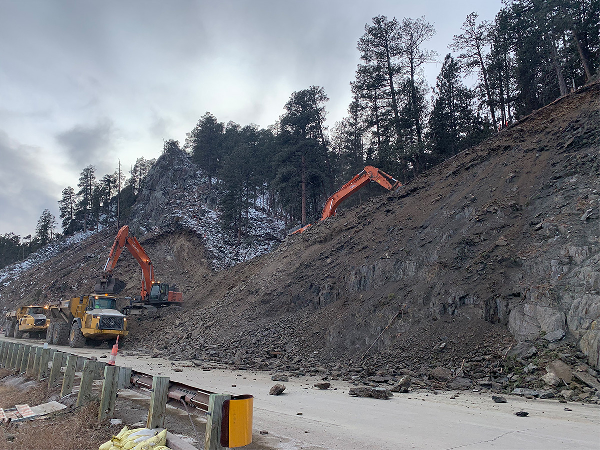 Construction equipment doing earth work on steep hill near roadway.
