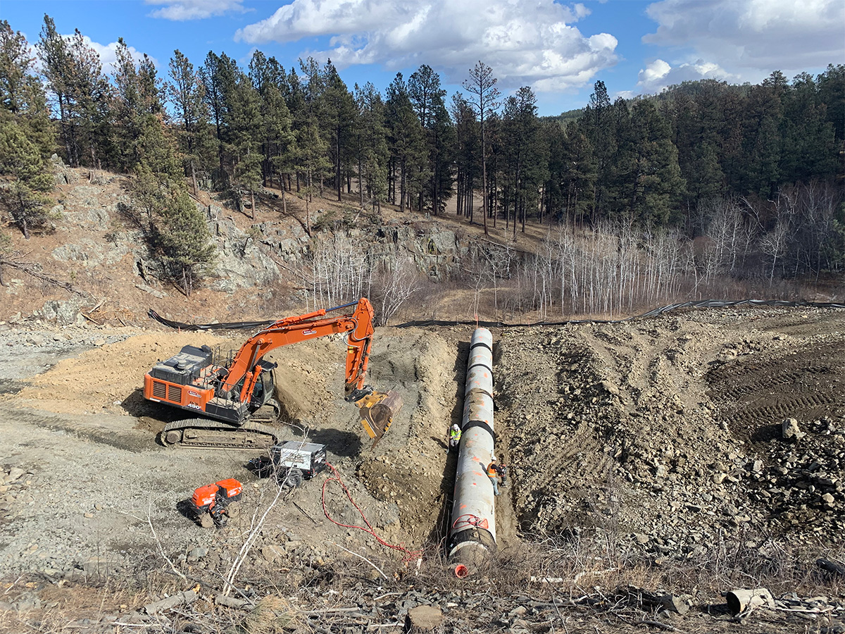 Machinery digging large trench and burying pipe/culvert.