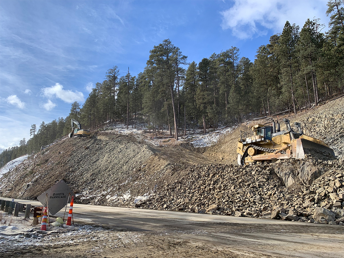 Bulldozer moving dirt and rock on a hill above the dirt roadbed.